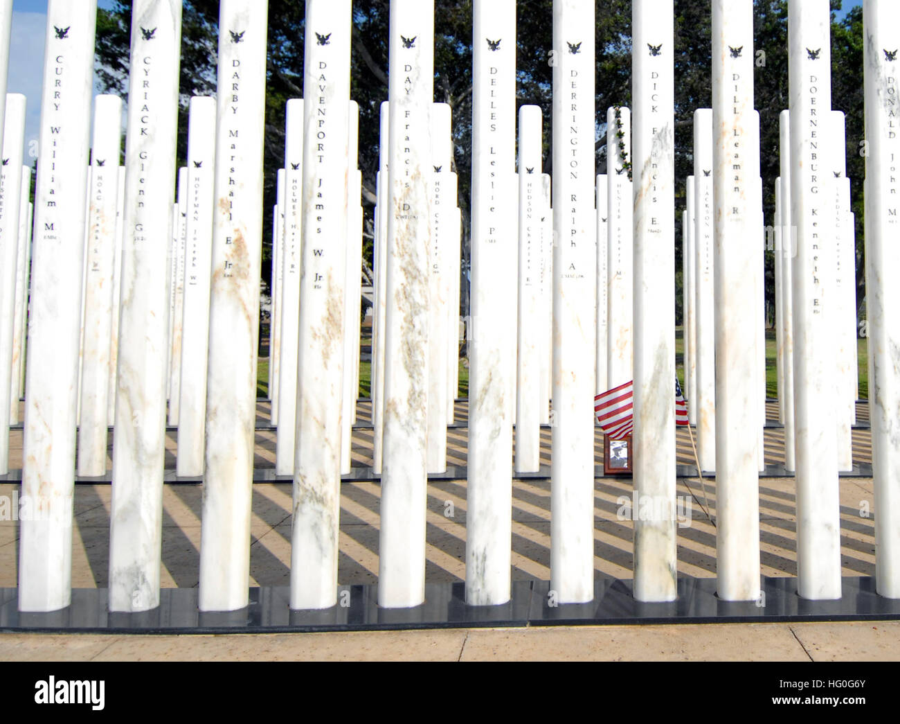 Eine US-Flagge und ein Foto stehen neben einem weißen Marmorsäule mit dem Namen eines gefallenen Matrosen während einer Zeremonie auf der USS Oklahoma Memorial 7. Dezember 2012, am gemeinsamen Basis Pearl Harbor-Hickam, Hawaii. Das Ereignis markiert den fünften Jahrestag der Gedenkstätte? s Engagement und zum 71. Jahrestag der Überraschung japanischen Angriff auf die US-Streitkräfte in Hawaii. Am Tag nach dem Angriff, vor einer gemeinsamen Sitzung des Kongresses, Präsident Franklin D. Roosevelt baten um eine Erklärung des Krieges gegen Japan und den USA offiziell trat während des zweiten Weltkriegs. Vier hundert neunundzwanzig Matrosen und Marinesoldaten starb, als t Stockfoto