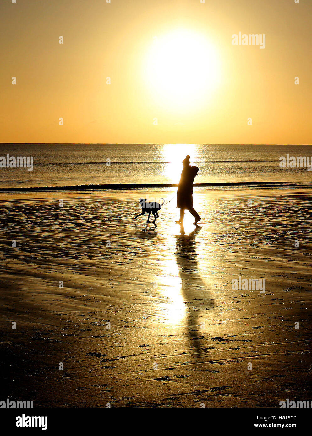 Eine Dame geht einen Hund am Strand wenn die Sonne untergeht in Camber, East Sussex, wie Teile des Vereinigten Königreichs von eisigen Bedingungen gepackt werden, wie eine Erkältung snap startet 2017. Stockfoto