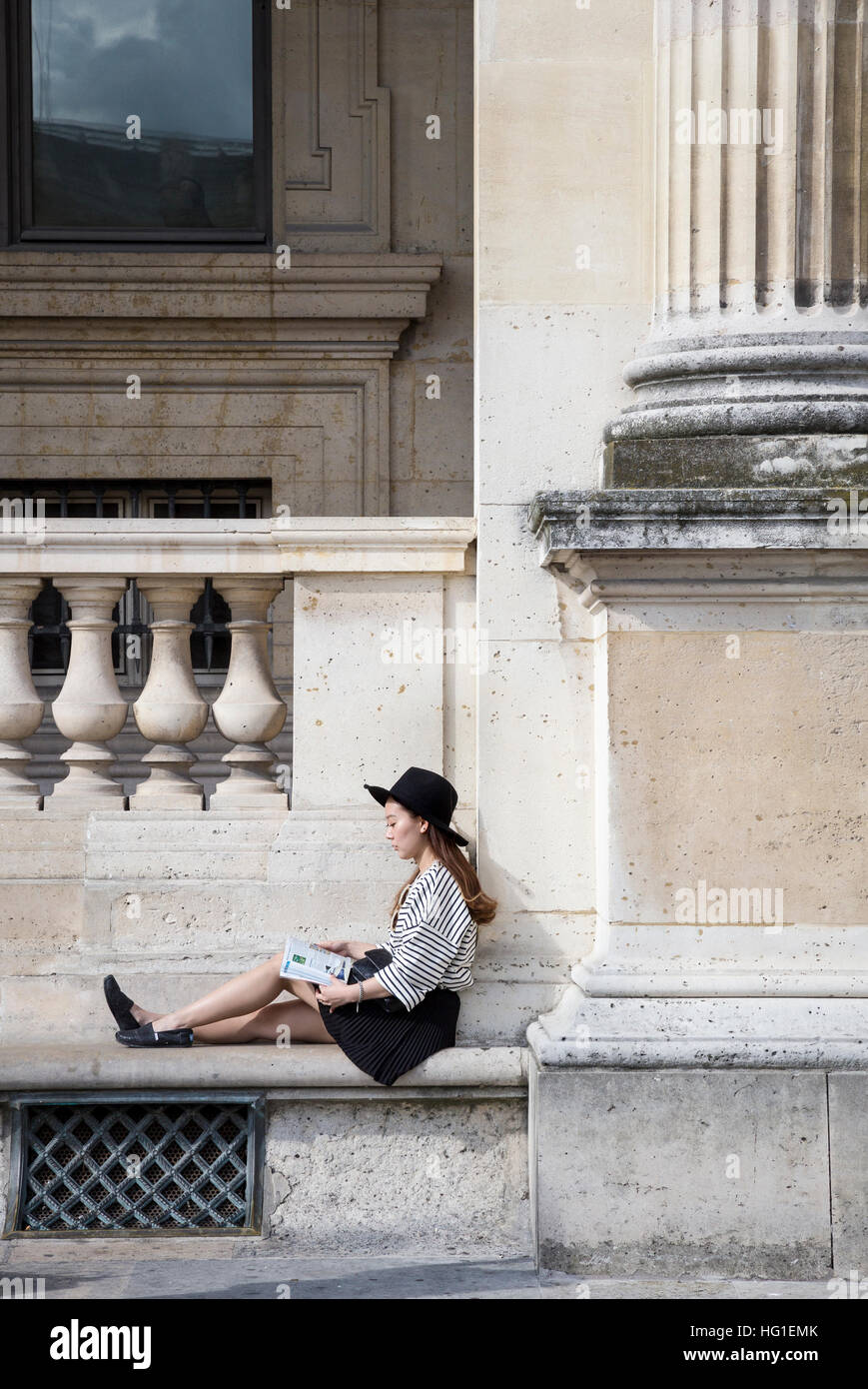 Modische asiatische Mädchen Lesen einer Zeitschrift an der Wand des Louvre in Paris, Frankreich Stockfoto