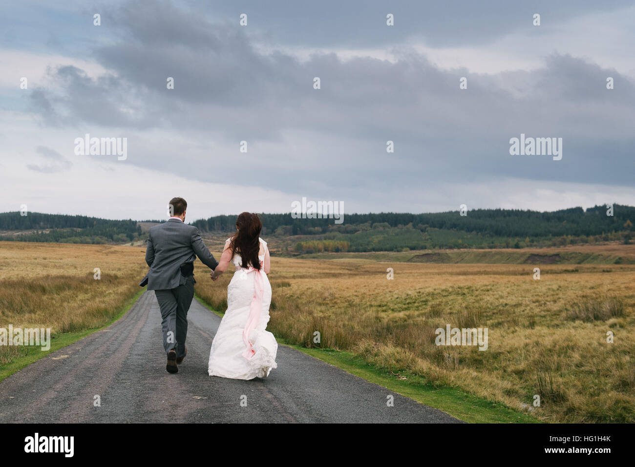 Ein paar Brautpaar laufen auf einer Straße in dramatischen Landschaft des Brecon-Beacons-Nationalpark, Wales, Großbritannien. Stockfoto