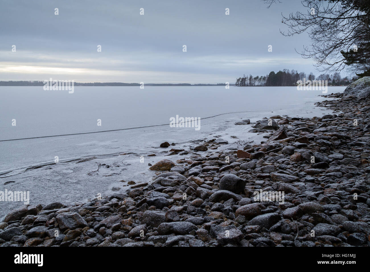 Schneebedeckten Felsen an einem Ufer und zugefrorenen und verschneiten See in Finnland in der Morgendämmerung im Winter. Stockfoto