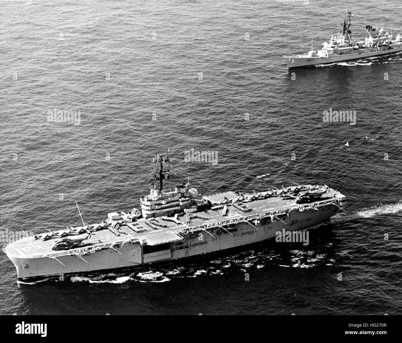 USS Guam (LPH-9) in den Indischen Ozean vor der Ostküste von Afrika, am 9. Dezember 1976 im Gange. Ihre Crew ist Kenia 76 auf dem Flugdeck in Verbindung mit ihrem Besuch in Mombasa, Kenia zur Feier der Unabhängigkeit des Landes bilden. USS Claude V. Ricketts (DDG-5) dampft in Unternehmen. Fotograf: PH3 Greg Haas, Atlantic Audio-visuelle Flottenkommando. Guam ist elf AV-8 Harrier Jet-Flugzeuge und zwei CH-53 Hubschrauber auf ihrem Flugdeck tragen.  Offizielle US-Navy, Foto, aus den Sammlungen der Marine-Geschichte und Erbe-Befehl. USS Guam (LPH-9) und USS Claude V. Ricketts (DD Stockfoto