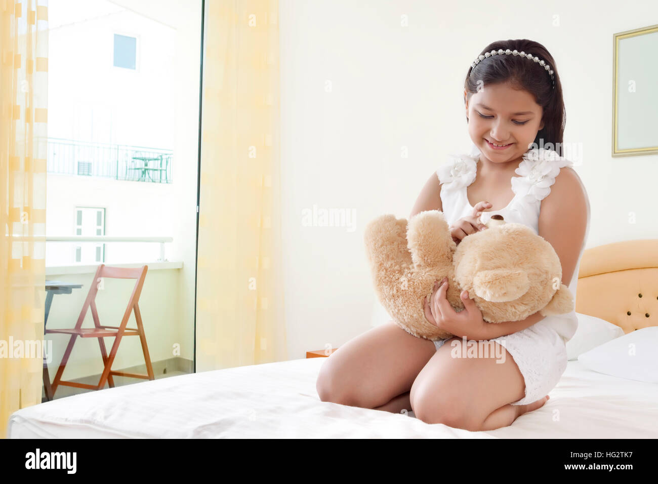 Glücklich lächelnde Mädchen spielen mit Teddybär auf dem Bett Stockfoto