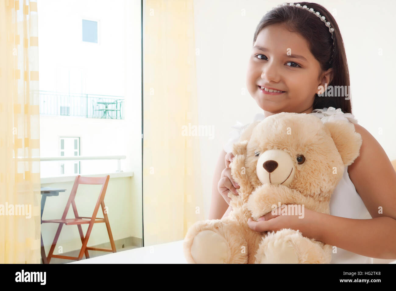 Glücklich lächelnde Mädchen spielen mit Teddybär auf dem Bett Stockfoto
