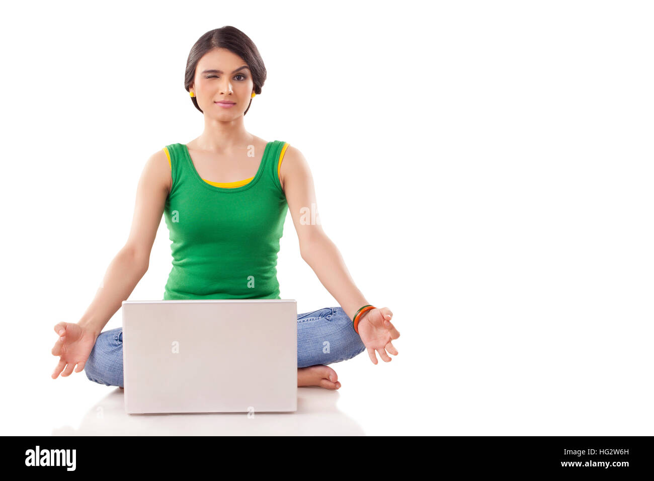 Junge Frau in Meditation Pose mit geschlossenen Augen und gekreuzten Beinen, während mit Blick auf einen Laptop vor. Auf weissem Hintergrund Stockfoto