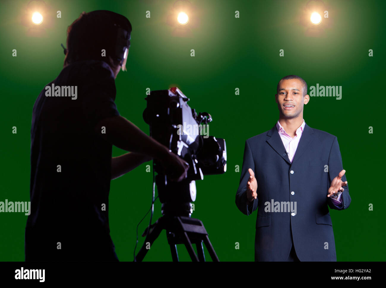 Moderator im Gespräch mit Kamera in einem Greenscreen-Studio mit Silhouette Kameramann im Vordergrund und Studio Lichter im Hintergrund. Stockfoto