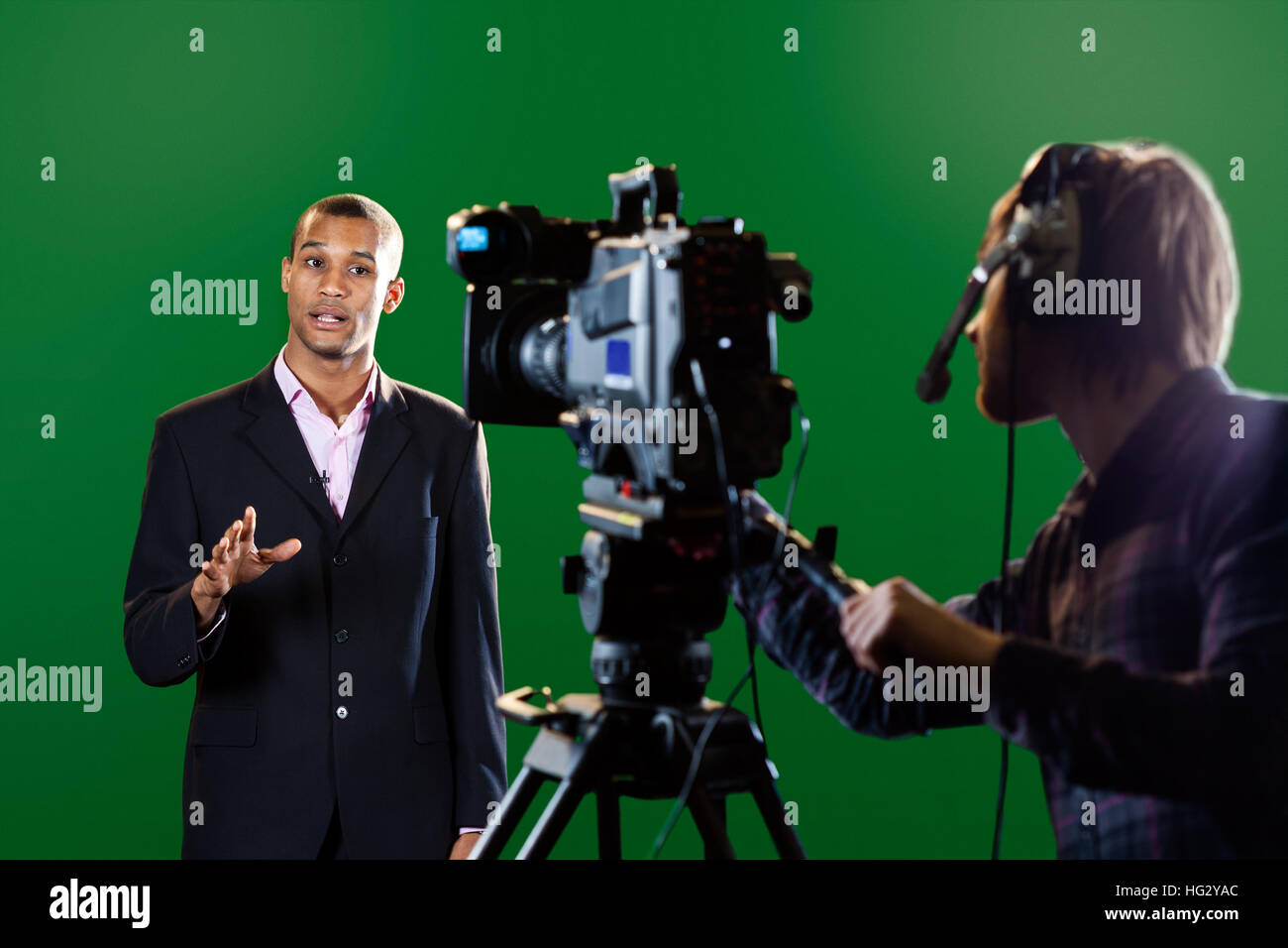 Eine TV-Moderatorin in einem TV-Studio mit einer Kamera und Betreiber unscharf im Vordergrund und einen grünen Bildschirm im Hintergrund. Stockfoto