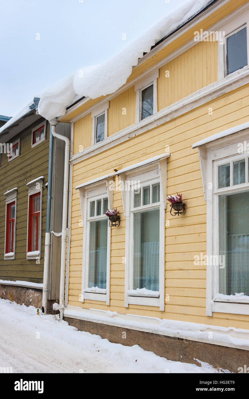 Schwere Last der Schnee hängen über eine Traufe von einem gelben Holzhaus im winter Stockfoto