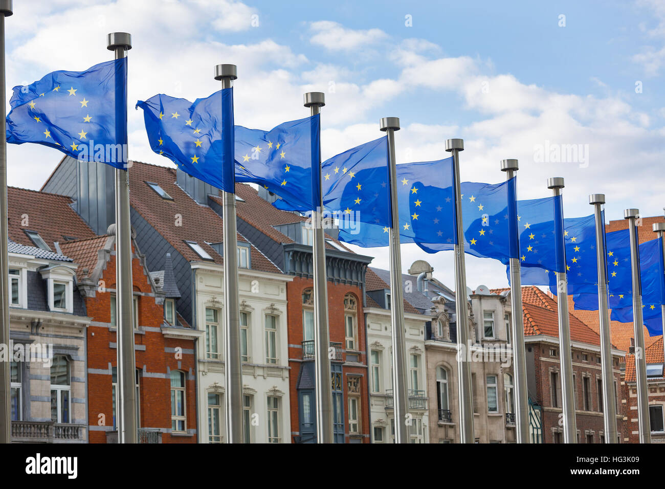 Eine Reihe von EU-Flaggen auf Metall Stangen vor dem Berlaymont-Gebäude in Brüssel mit traditionellen Häusern im Hintergrund fliegen. Stockfoto