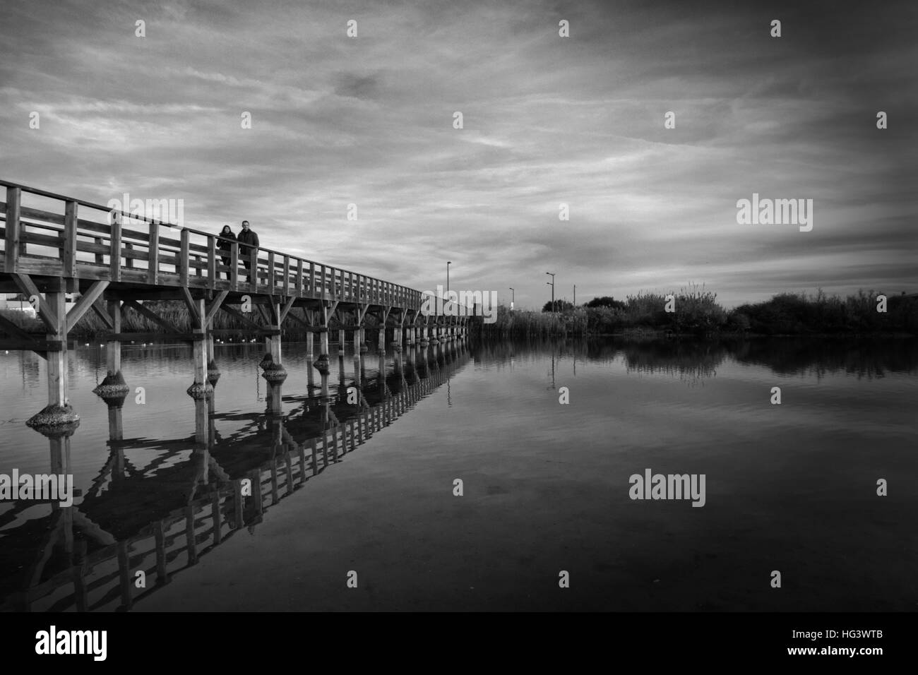 BW-Foto der Holzbrücke mit Menschen zu Fuß spiegeln Wasser Stockfoto