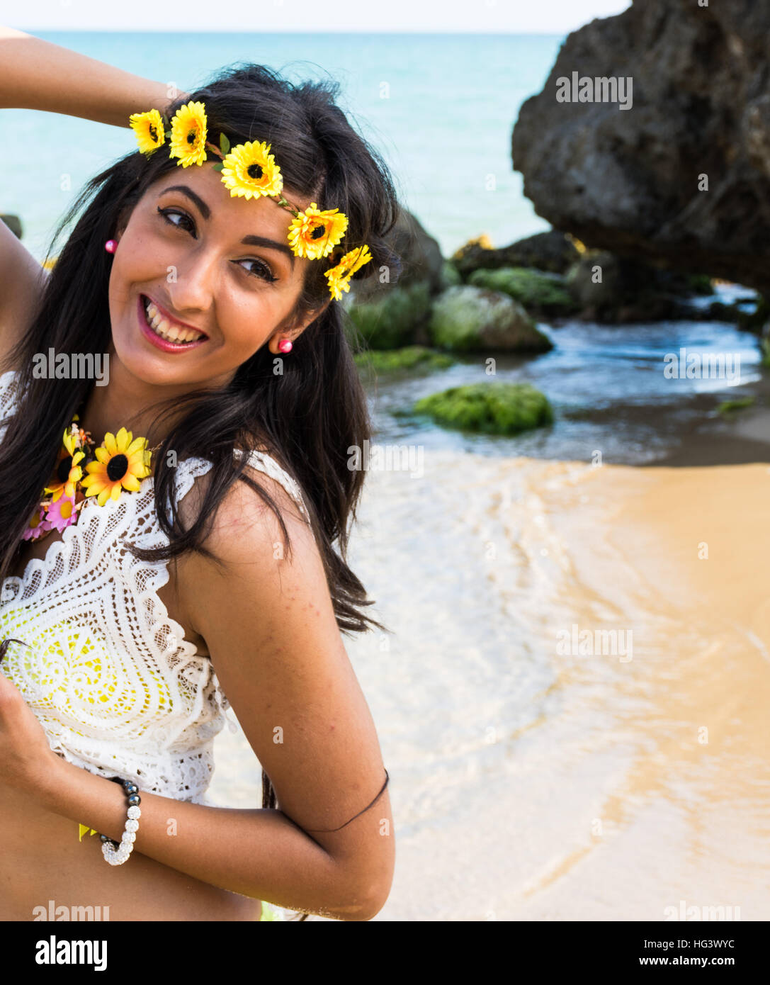 Mädchen am Strand mit Krone aus Blumen gelb Badeanzug. Glücklich und lächelnd, Sonnenbaden, Sonnenbaden, Strand zwischen den Felsen. Stockfoto
