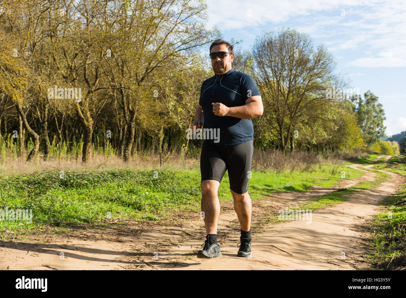 Dicken Bauch Mann Joggen, Sport treiben, tun, Cardio im Park, leicht übergewichtig, Gewicht zu verlieren. Auf einer Wiese grüne Gras zwischen den Bäumen ohne lea Stockfoto