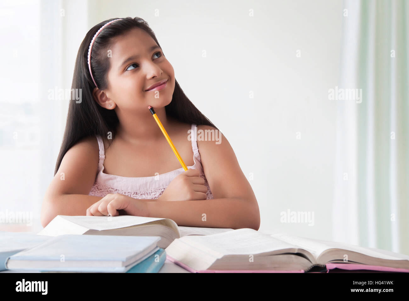 Porträt der lächelnde niedliche Mädchen denken am Schreibtisch mit Bücher Stockfoto