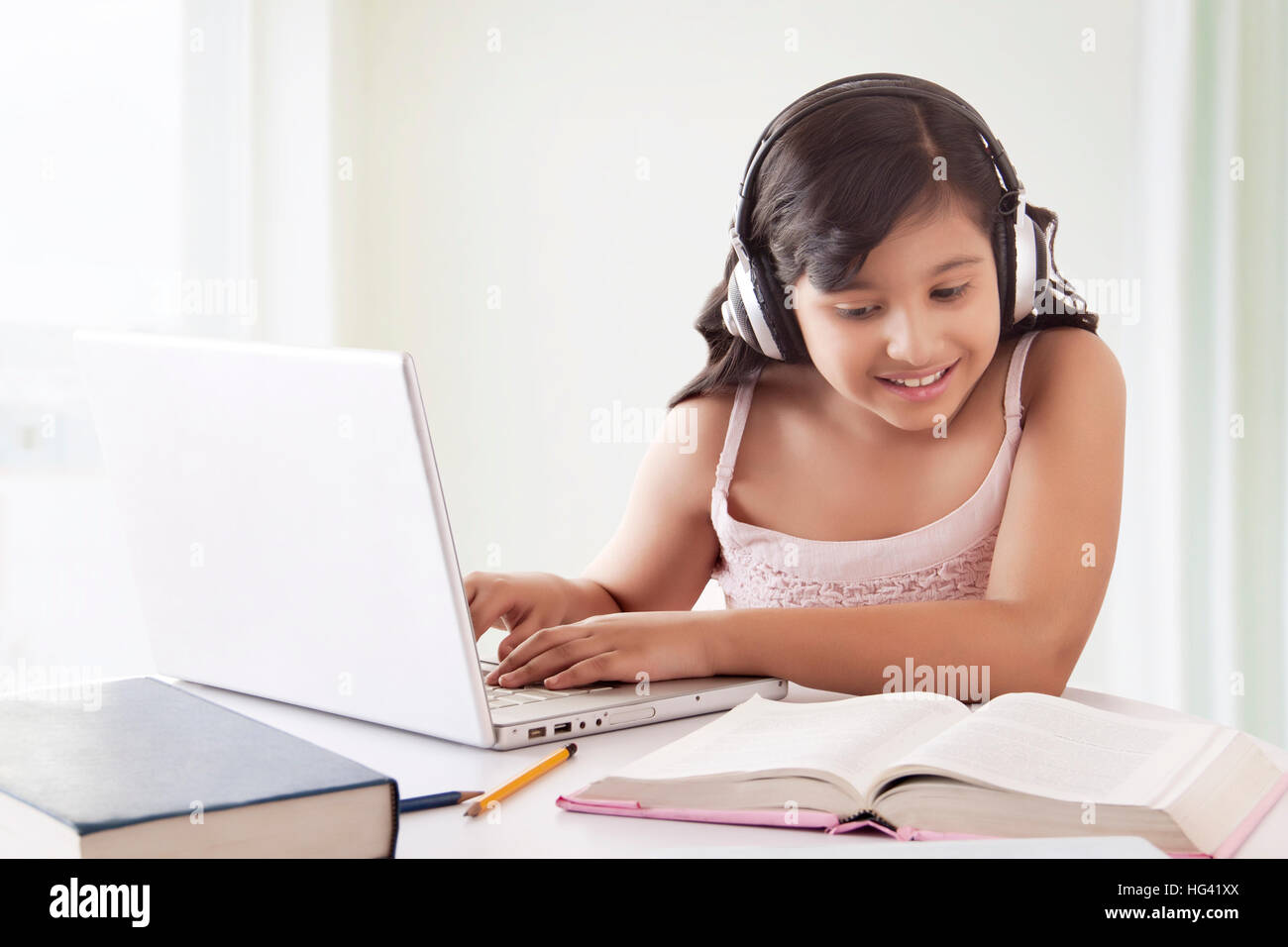 Porträt der lächelnde niedliche Mädchen das Tragen von Kopfhörern während mit Laptop und suchen zum Lehrbuch Stockfoto