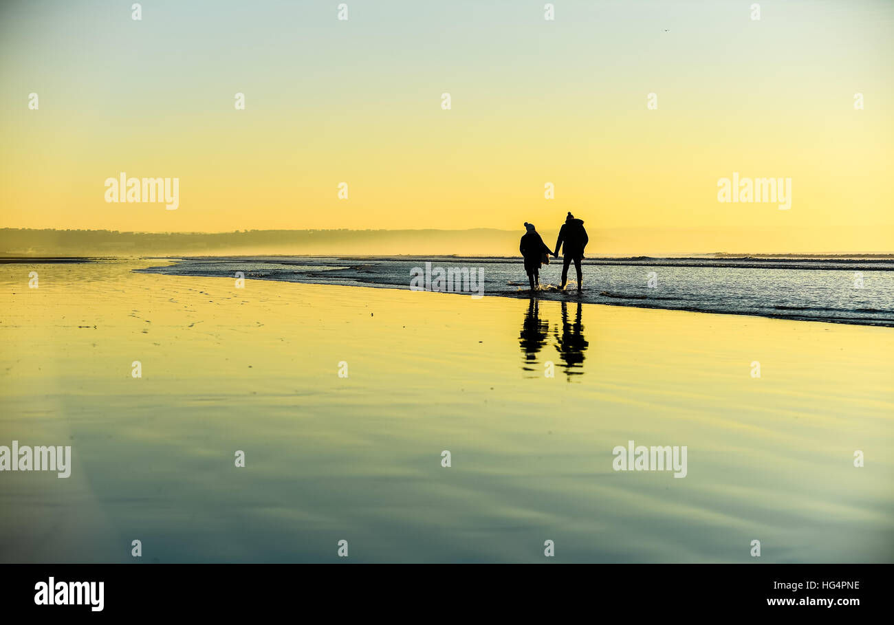 Ein junges Paar in Liebe Hand in Hand am Strand bei Sonnenuntergang. Stockfoto
