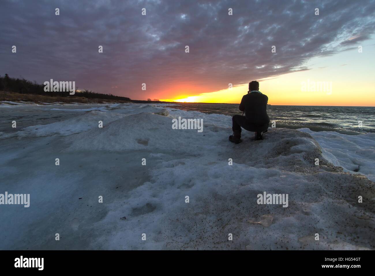 Männlichen Fotografen auf einem zugefrorenen See. Junge männliche Fotografen kniend am Ufer des zugefrorenen Küste. Hafen Austin, Michigan. Stockfoto