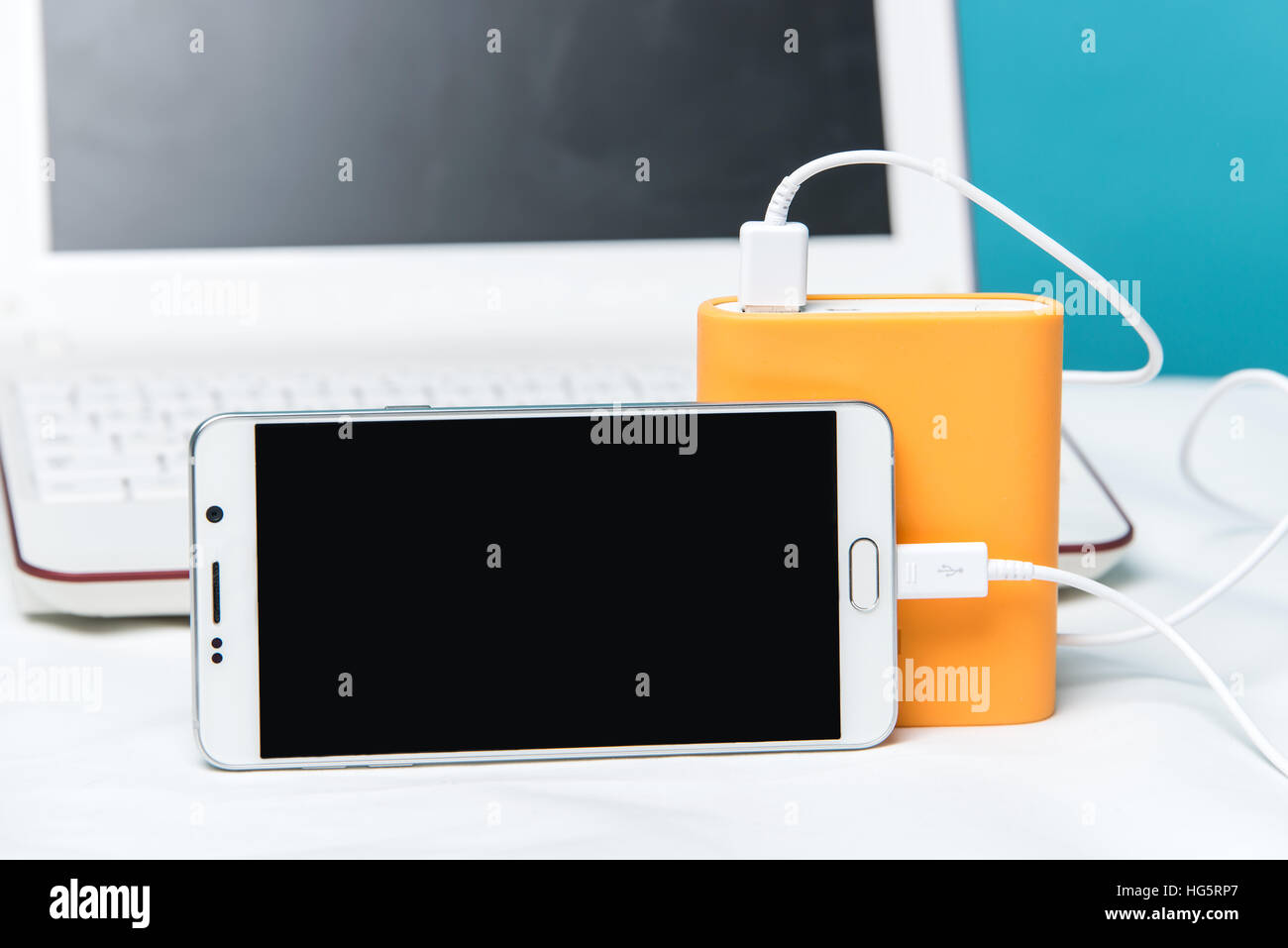 Smartphone laden mit tragbaren externen Batterie auf modernen Laptop im Hintergrund. Stockfoto