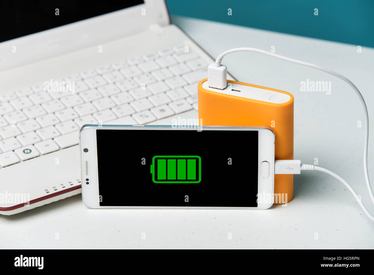 Voller Ladung eines Smartphones auf den Monitor mit dem Kabel verbunden, die spezielle Powerbank. Moderne Laptop im Hintergrund. Stockfoto