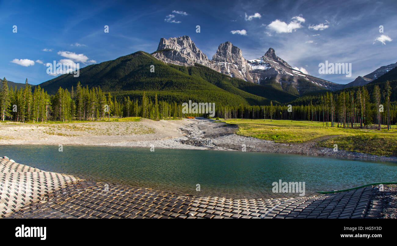 Three Sisters Mountain Peak, Panoramalandschaft im Grünen Wald mit blauer Skyline und Reservoir im Vordergrund. Canmore, Alberta, Kanadische Rockies Stockfoto