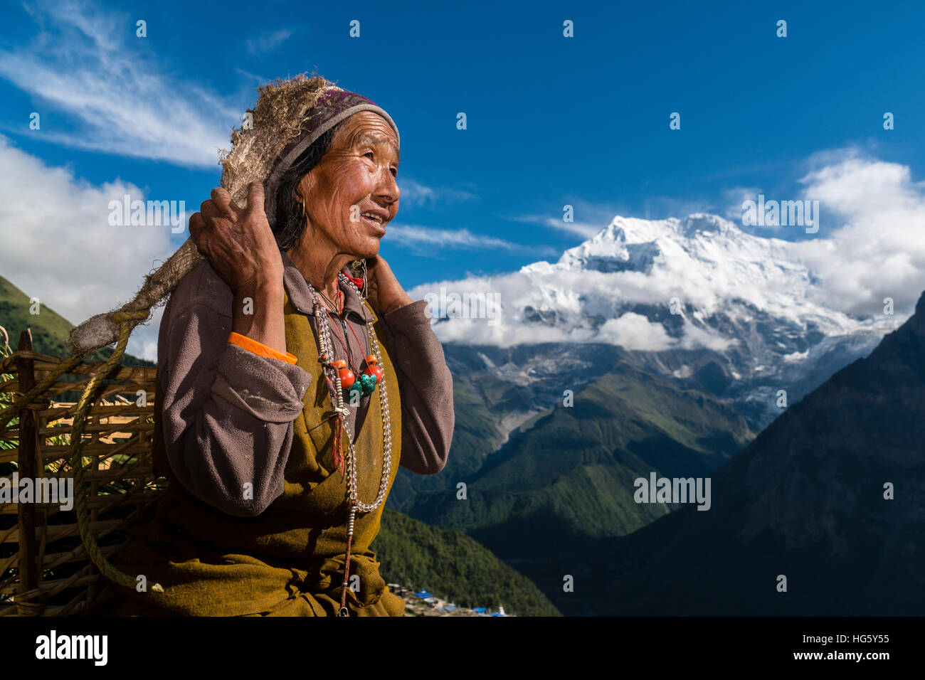 Bäuerin mit Korb mit Erntegut mit Mount Annapurna II in der Entfernung, Ghyaru, Manang Bezirk, Nepal Stockfoto