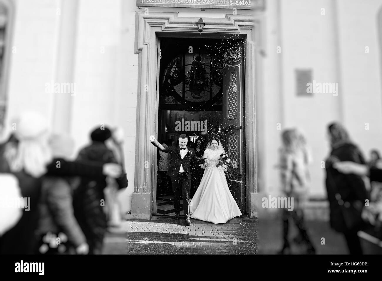 Gäste geduscht Brautpaar mit bunten Reis nach der Trauung in der Kirche. Schwarz / weiß Foto Stockfoto