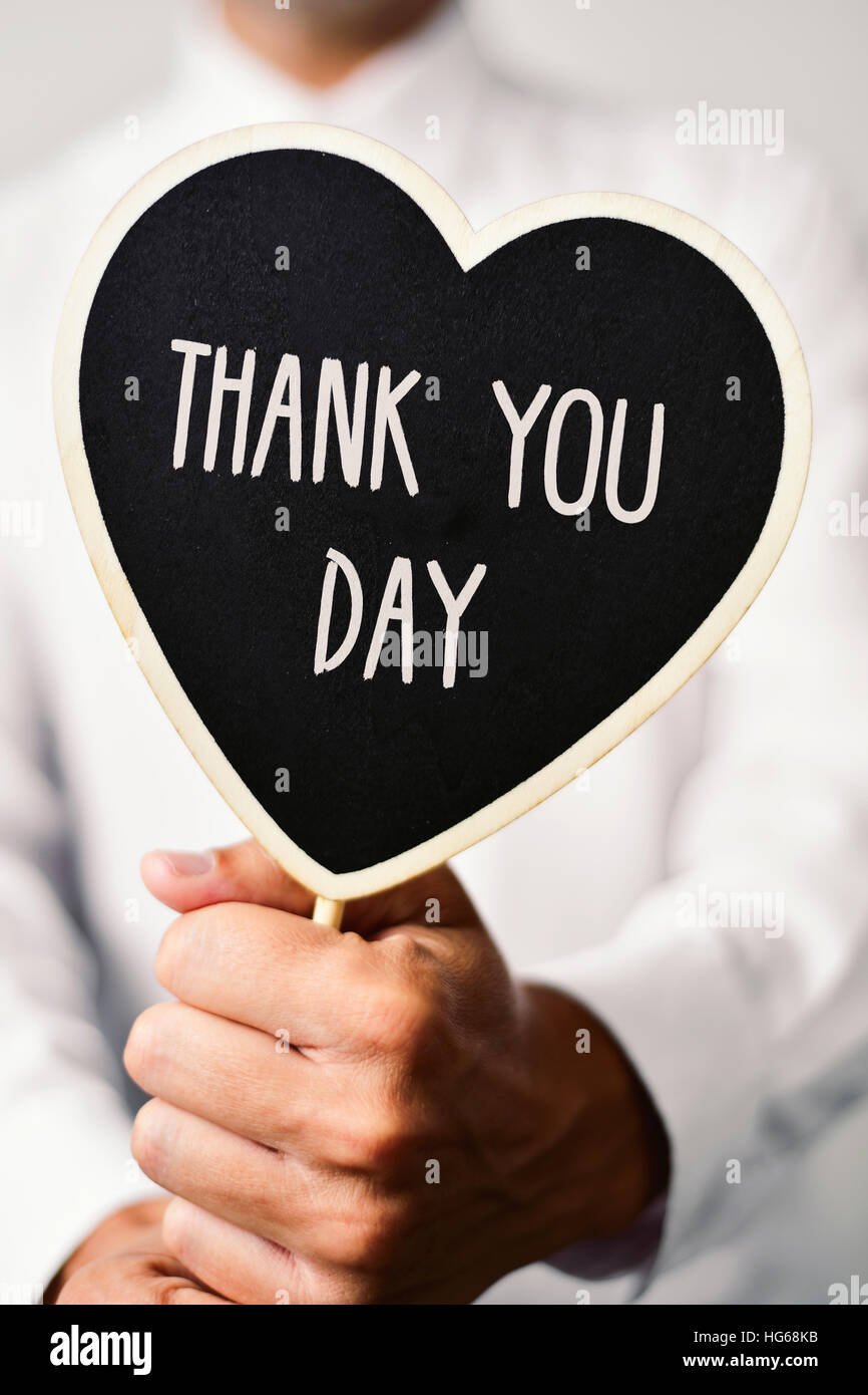 ein junger kaukasischer Mann trägt ein weißes Hemd zeigt ein herzförmiges Schild mit dem Text-Danke-Tag geschrieben Stockfoto