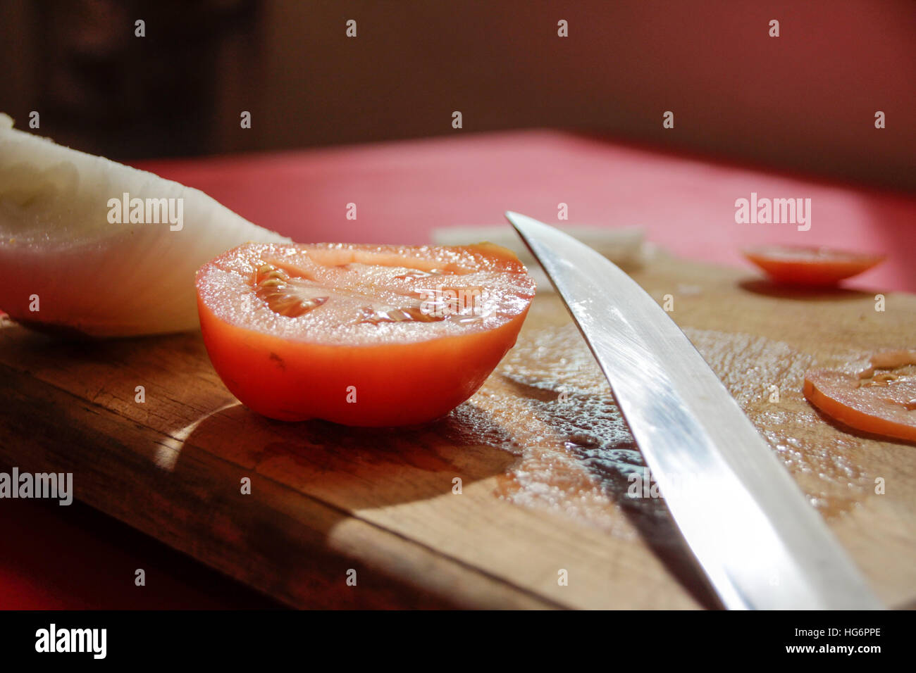 Foto von einem Messer, Tomatenscheiben und Zwiebeln auf ein Holz Schneidebrett Stockfoto