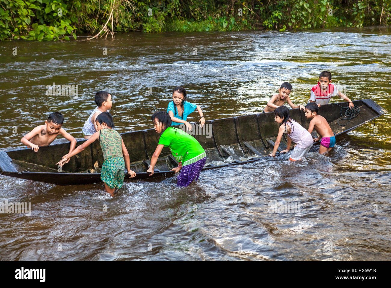 Kinder, die sich mit einem Holzboot in einem Fluss in der Nähe des Langhauses der traditionellen Dayak IBAN-Gemeinde in Kapuas Hulu, Indonesien, erholen. Stockfoto