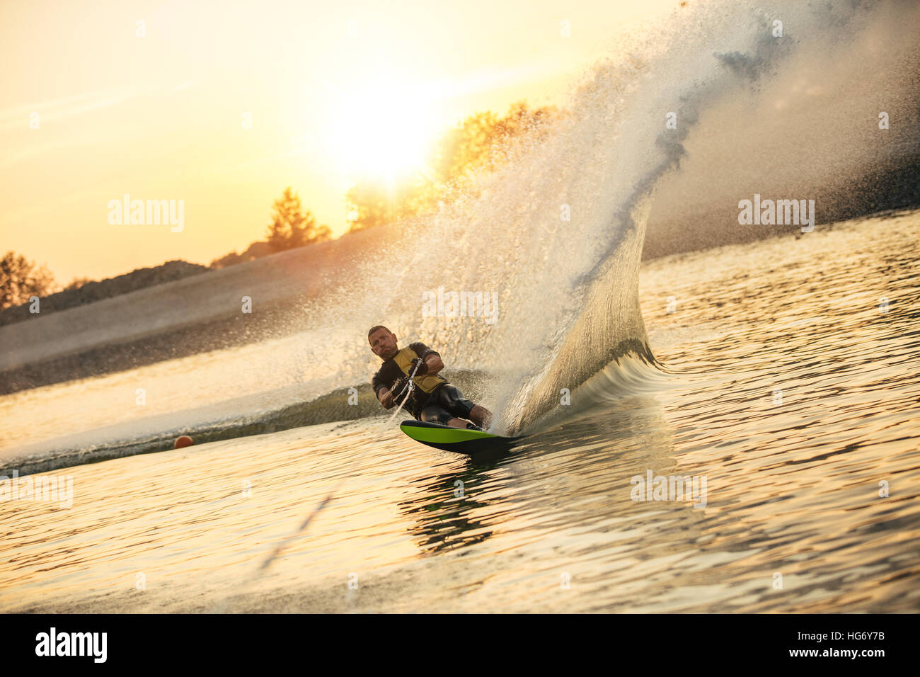 Wasserschifahrer bewegt sich schnell in Spritzwasser bei Sonnenuntergang. Mann Wakeboarden auf einem See Stockfoto
