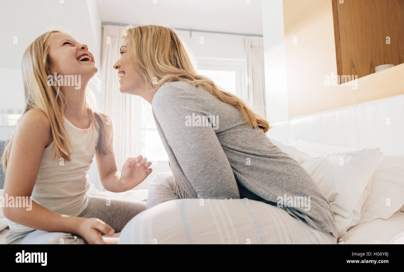 Schuss von junge Frau und kleine Mädchen am Bett sitzen und lachen. Mutter und Tochter im Schlafzimmer genießen. Stockfoto