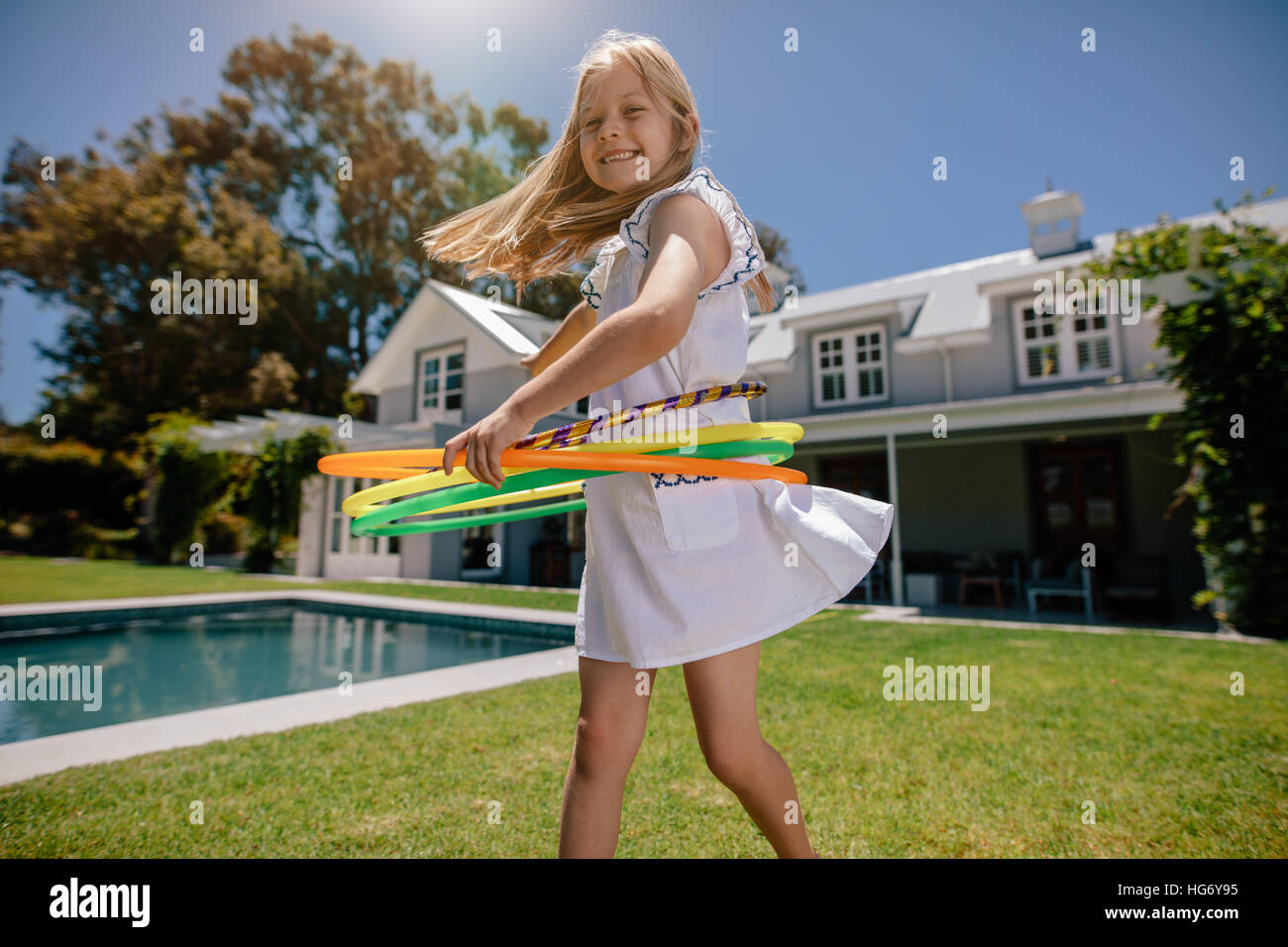 Glückliche kleine Mädchen spielen mit Hula-Hoop im Hinterhof. Lächelndes Mädchen spielen im Freien an einem Sommertag. Stockfoto