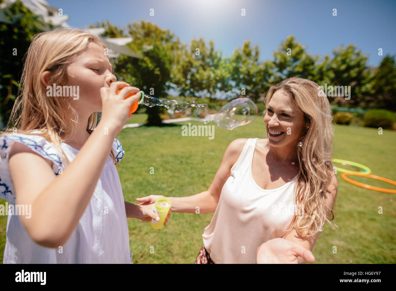 Kleines Mädchen bläst Seifenblasen mit der Mutter lächelnd im Park. Mutter und Tochter genießen einen Tag im Park. Stockfoto