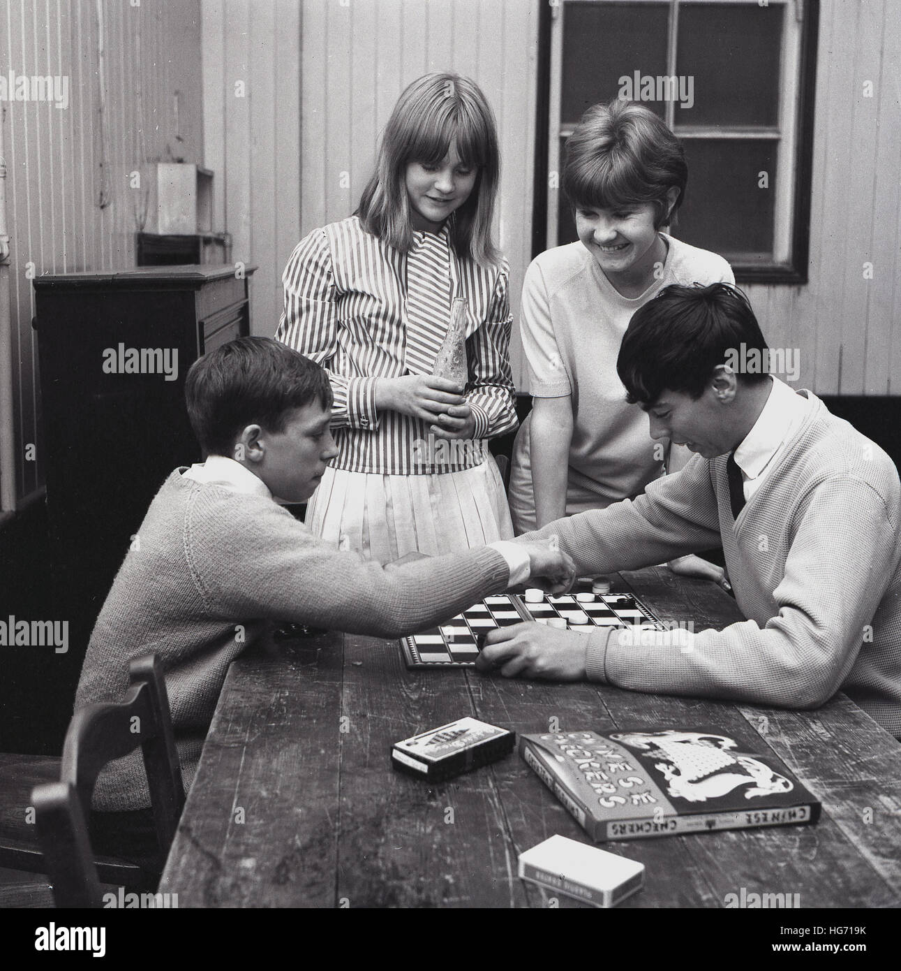 1960er-Jahren, historische, zwei Jungs sitzen an einem Tisch mit zwei Mädchen auf der Suche auf, "Englische Zugluft", ein strategisches Brettspiel, mit einem anderen Brettspiel, "Chinese Checkers" spielen auf dem Tisch. Stockfoto