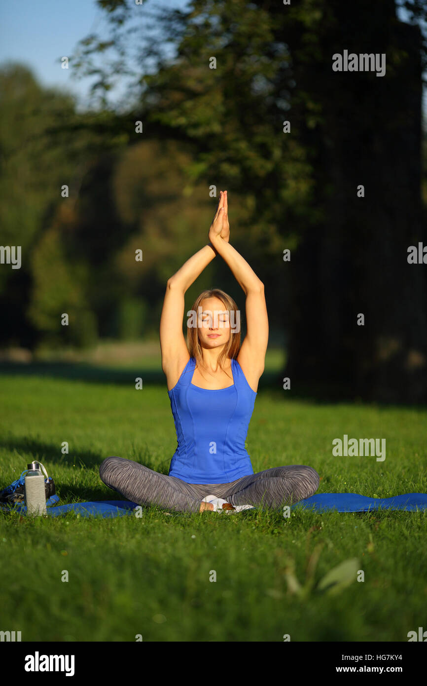 Junge Frau sitzt auf Yoga-Matte mit Händen oben die hatte im Wald Stockfoto