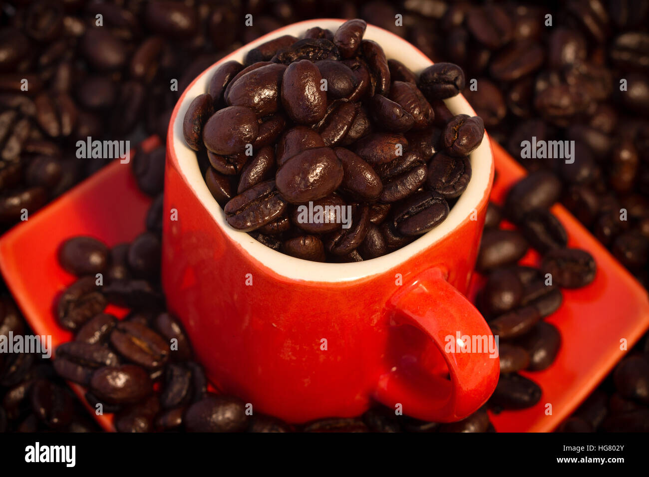 Dunkel geröstete Kaffeebohnen in und um orange Espressotasse. Stockfoto