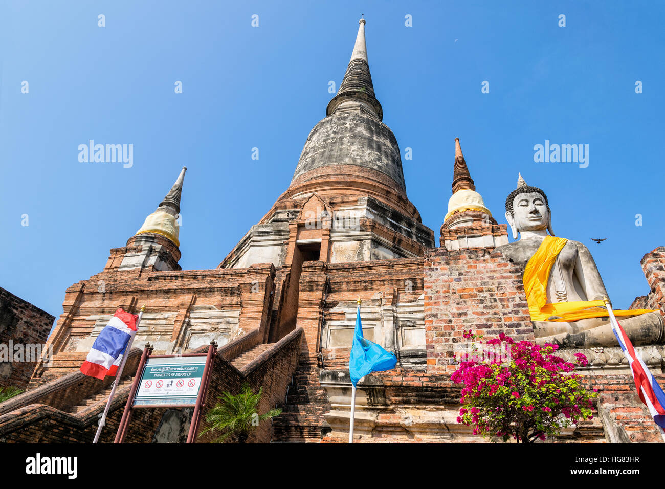 Buddha-Statue am unteren Rand eine große alte Pagode auf blauen Himmelshintergrund am Wat Yai Chai Mongkon Tempel in Phra Nakhon Si Ayutthaya Historical Stockfoto