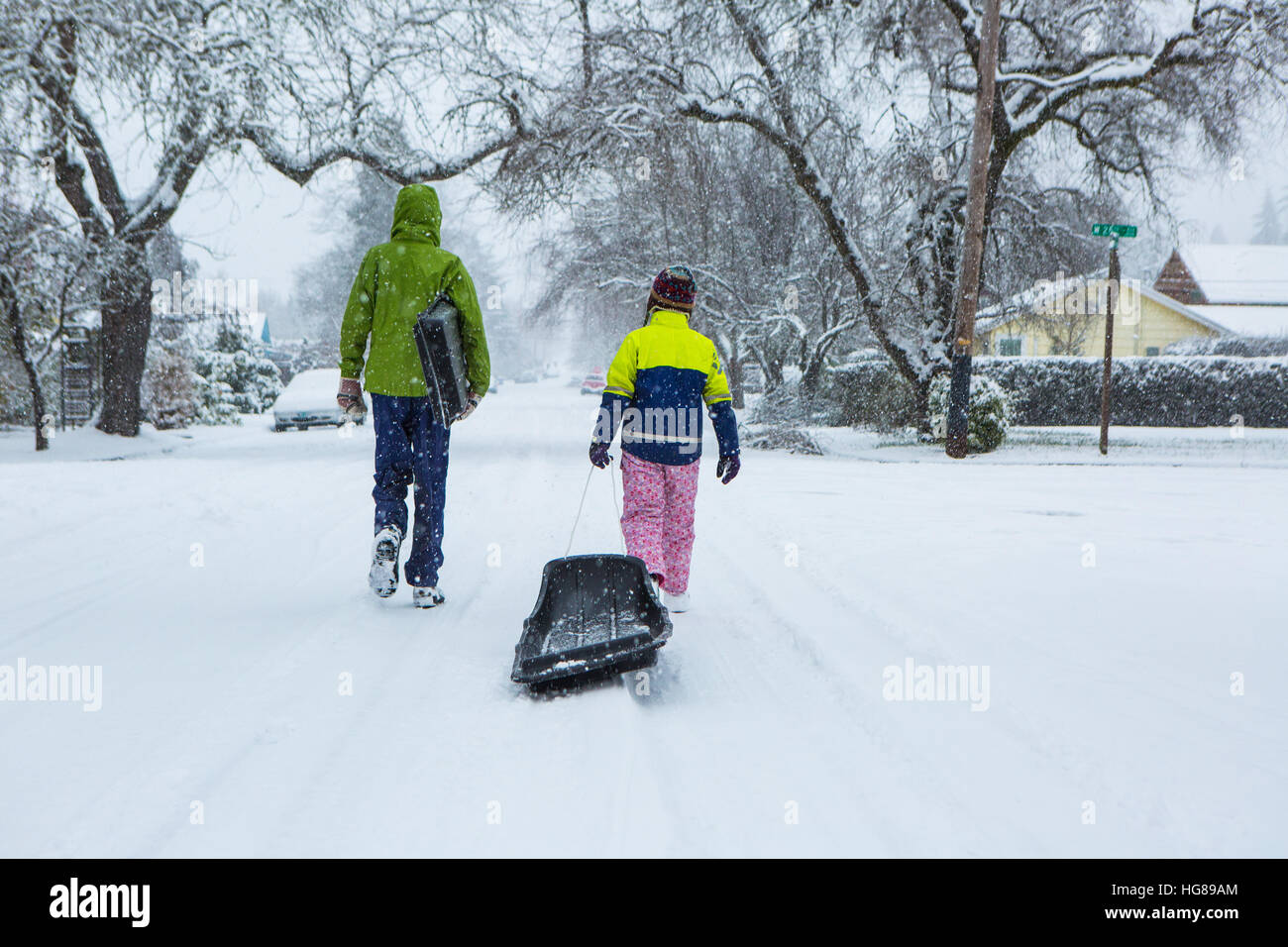 Kinder Fuß hinunter die Mitte einer leeren Straße ziehen Schlitten im frisch gefallenen Winterschnee. Stockfoto