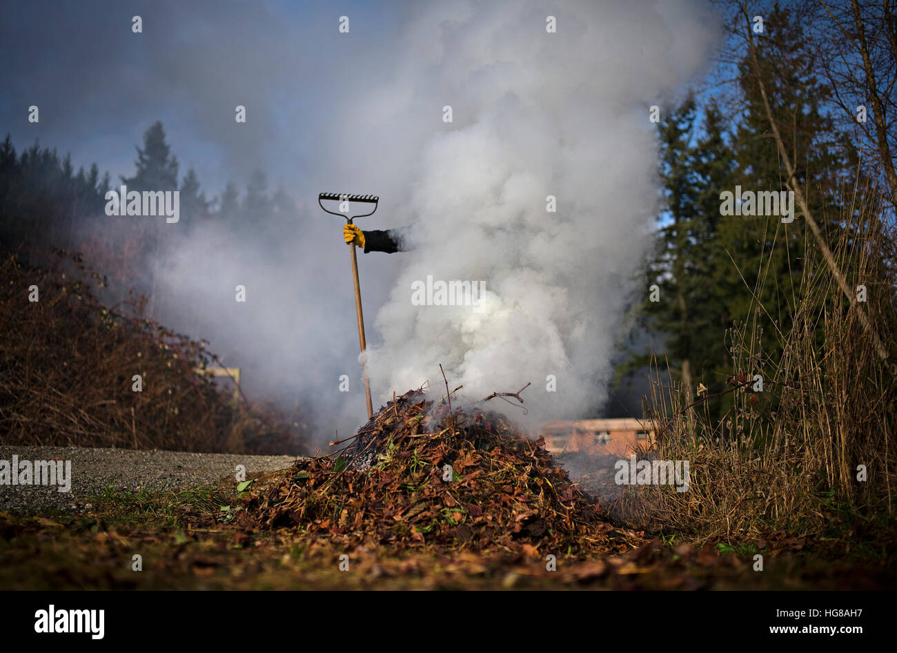 Person mit Gartengeräten von Rauch ausstoßen von verbrannten Blättern umgeben Stockfoto