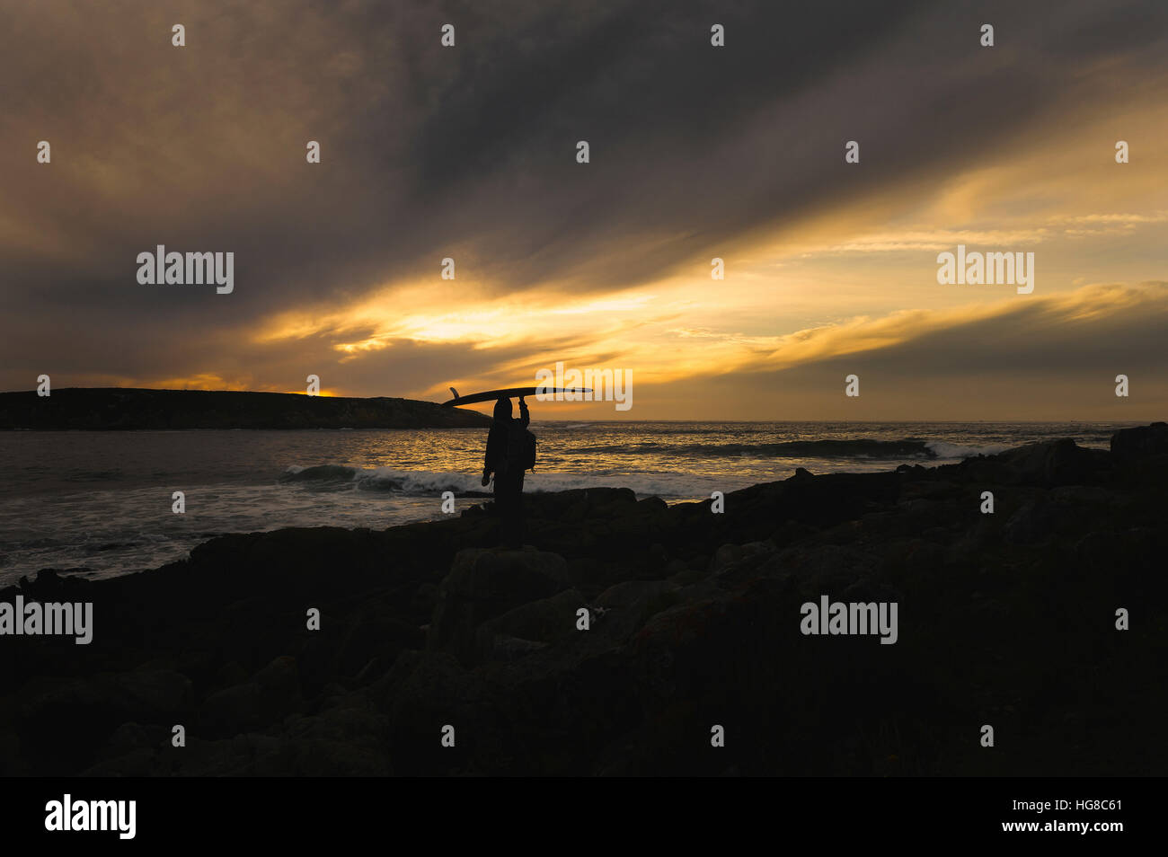 Silhouette Mann mit Surfbrett auf Kopf im stehen am Strand bei Sonnenuntergang Stockfoto