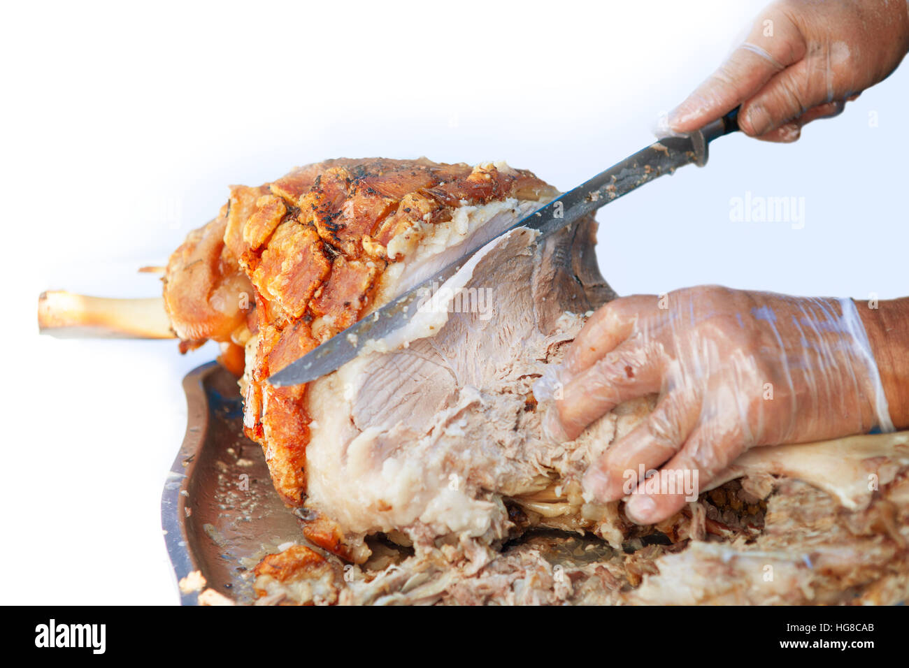 Hand eines Mannes mit Messer schneidet Scheiben von geröstetem Schweinefleisch Stockfoto