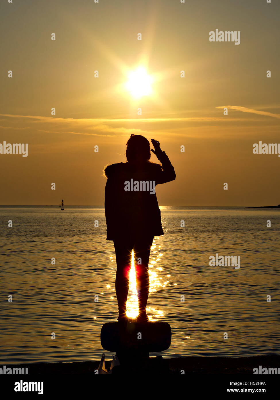 Silhouette einer Frau auf Poller am Meer Sonnenuntergang Hafen stehen. Stockfoto