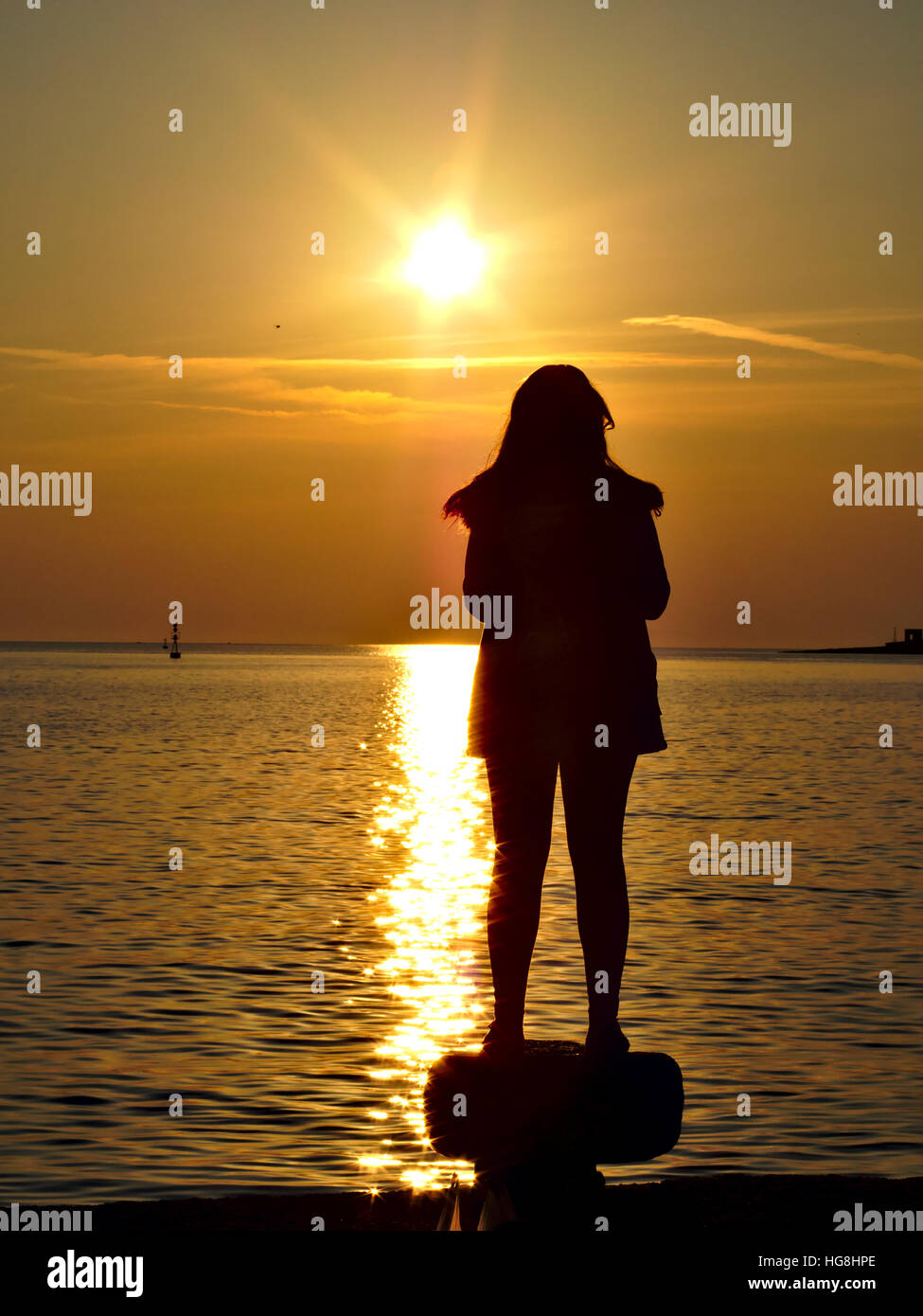 Silhouette einer Frau auf Poller am Meer Sonnenuntergang Hafen stehen. Stockfoto