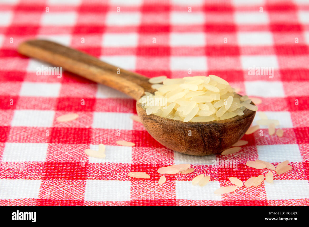 Rohe parboiled-Reis in einem Holzlöffel auf karierten Tischdecke Stockfoto