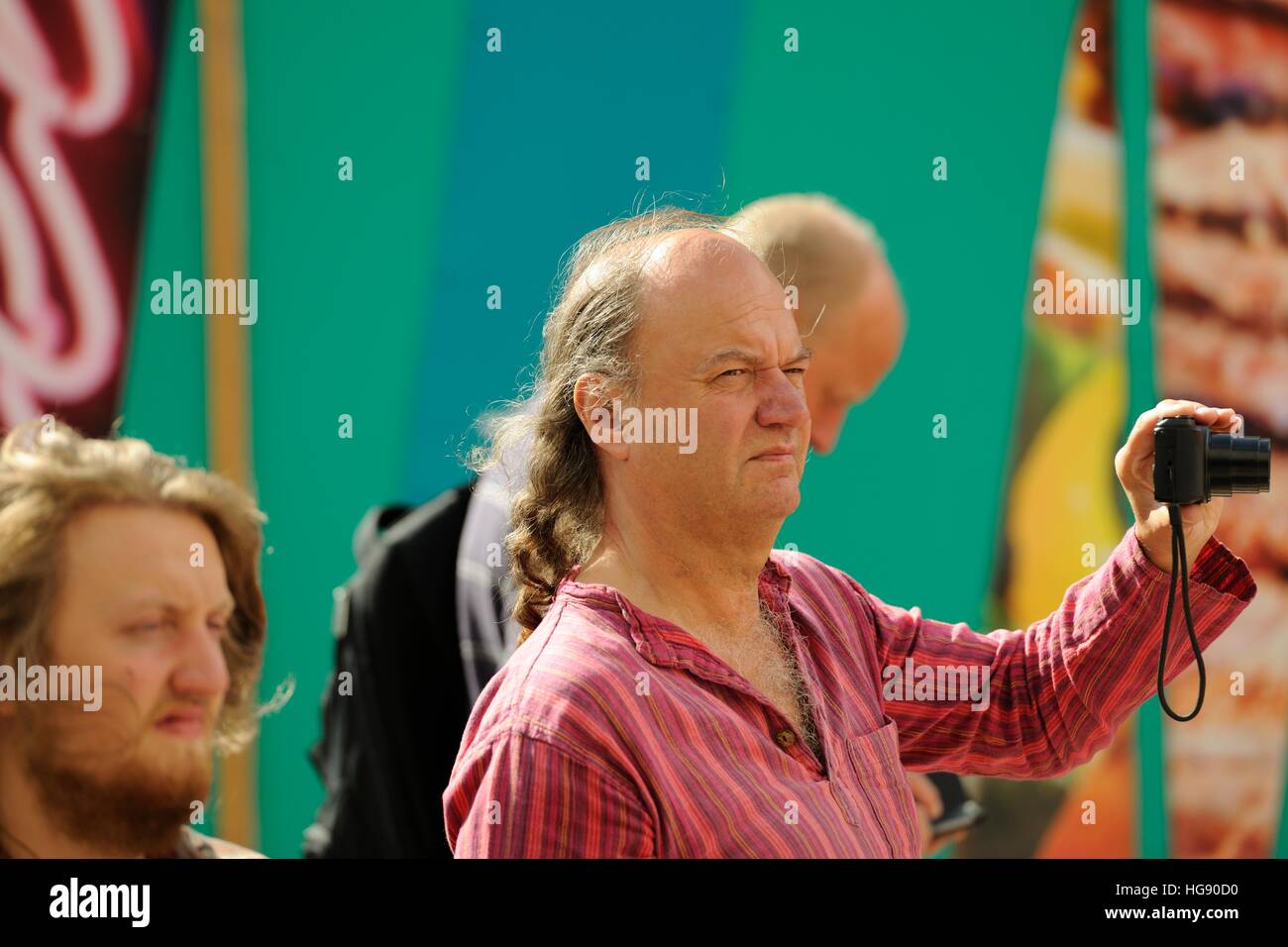 Mann mittleren Alters mit langen Haaren, die Aufnahme eines Bildes mit einer Kompaktkamera, Straßenbahnlinien Festival Fringe, das Moor, Sheffield 2014 Stockfoto