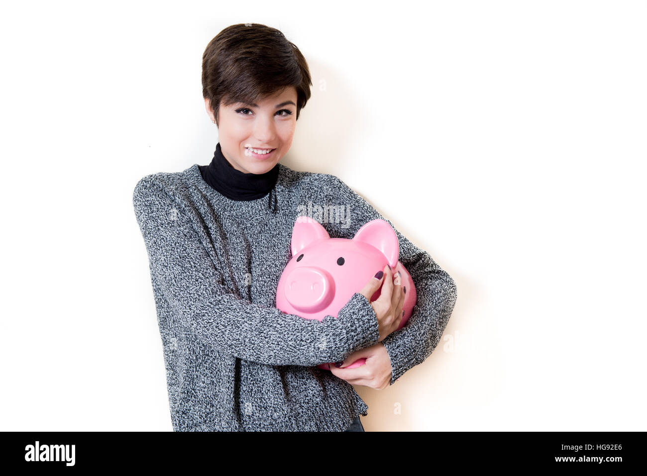 Junge Frau glücklich umarmt ein Sparschwein mit Einsparungen, Blick in die Kamera und lächelnd auf weißem Hintergrund isoliert textfreiraum auf der rechten Seite Stockfoto
