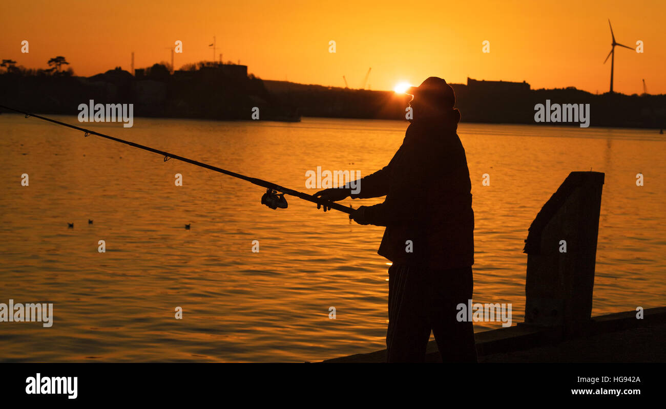 Ein Fischer bei Sonnenuntergang wirft seine Rute und Schnur in der Hoffnung auf einen Fisch fangen. Die Sonne ist fast verschwunden, da das letzte Licht ist Stockfoto
