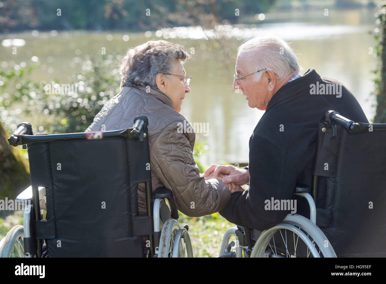 Älteres Ehepaar im Rollstuhl, für einander zu erreichen Stockfoto