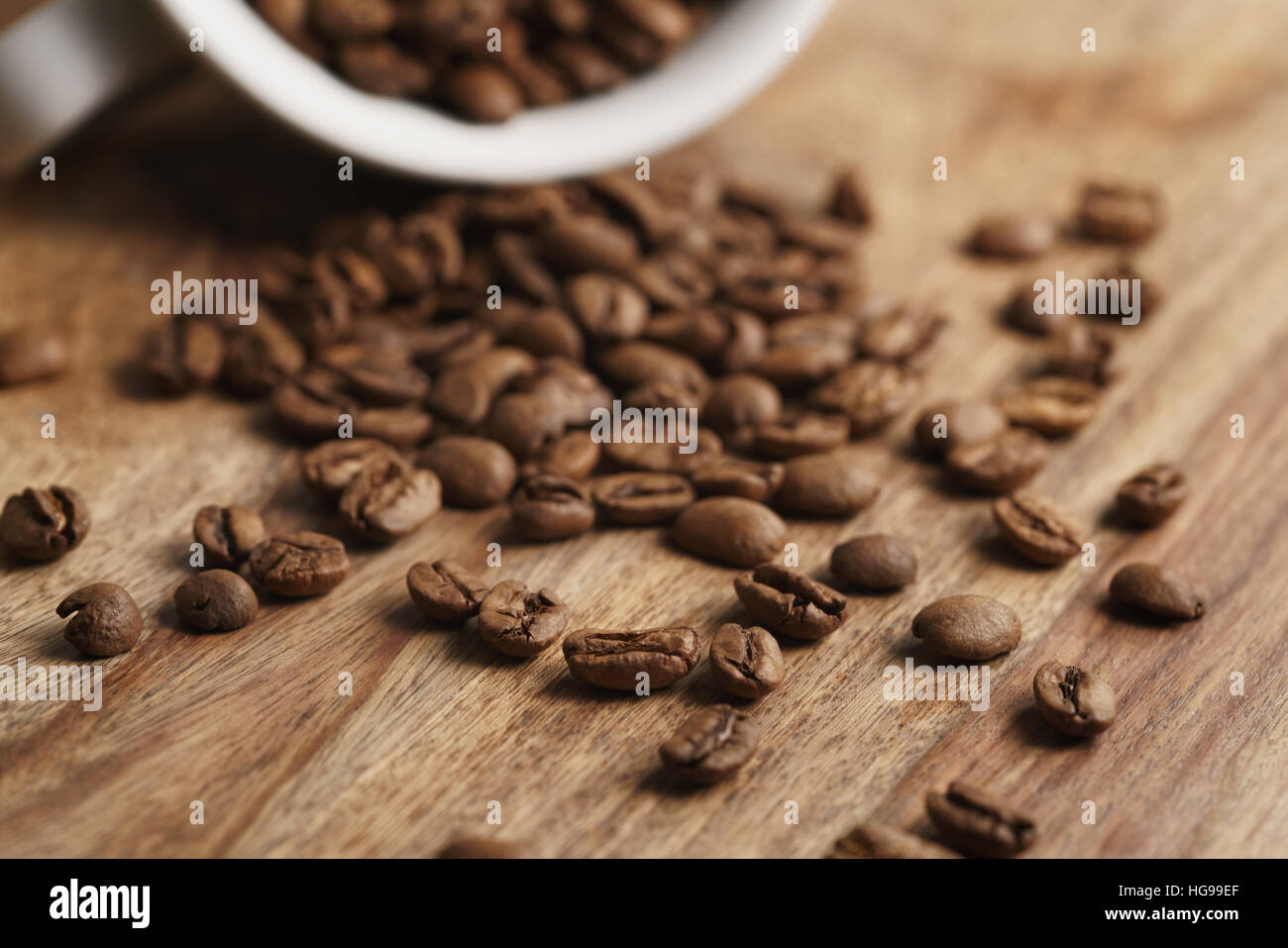 umgestürzten Cappuccino-Tasse mit geröstete Kaffeebohnen auf Holztisch Stockfoto