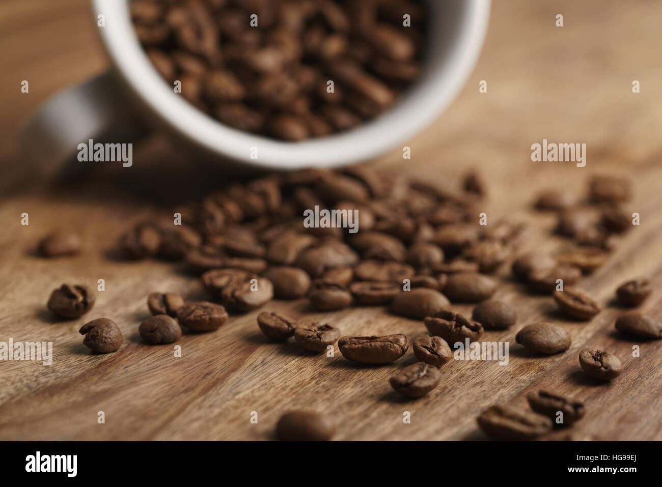 umgestürzten Cappuccino-Tasse mit geröstete Kaffeebohnen auf Holztisch Stockfoto