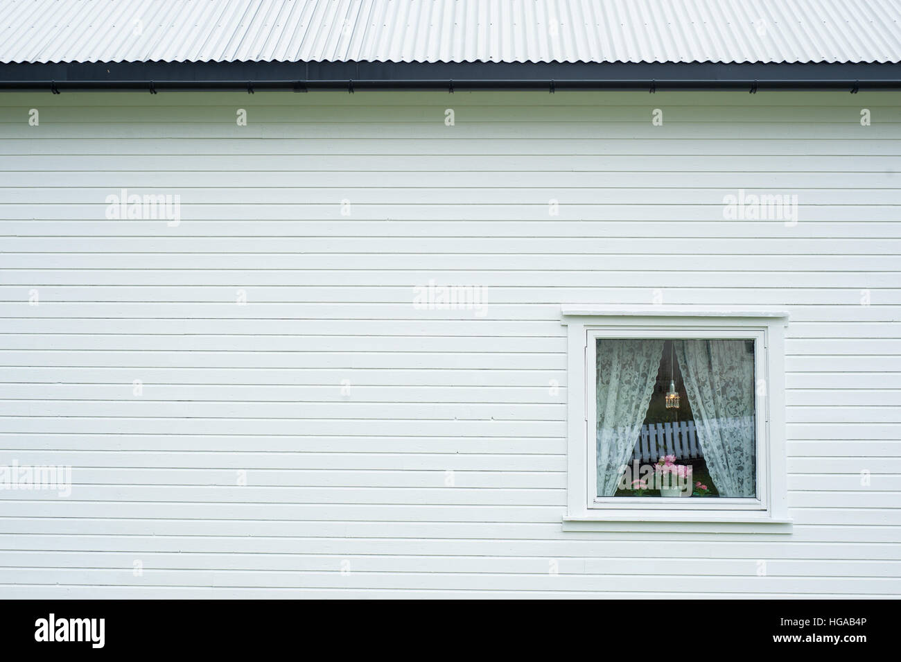 Seitenansicht eines weißen Holzhauses mit kleinen Fenster mit Vorhängen und Blumen Stockfoto